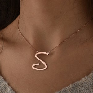 Puede incluir: Un collar de oro rosa con un colgante de la letra 'S' en cursiva.