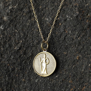 May include: A gold necklace with a round pendant featuring a detailed image of a woman holding a spear and a shield.