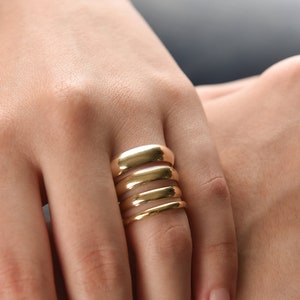 May include: A close-up of a hand wearing five gold stacking rings. The rings are all different sizes and widths, and they are stacked on top of each other.