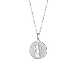 May include: A silver necklace with a round pendant featuring a stylized image of a woman holding a staff and a shield. The pendant has a textured surface.