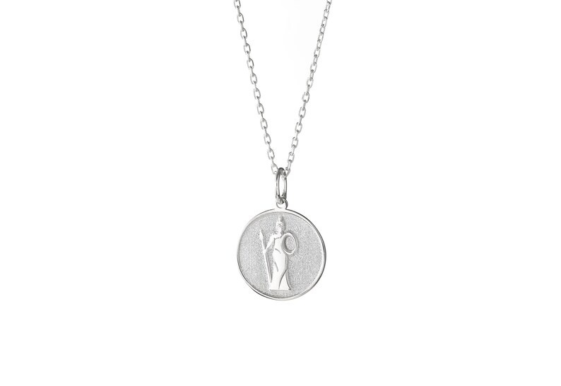 May include: A silver necklace with a round pendant featuring a stylized image of a woman holding a staff and a shield. The pendant has a textured surface.