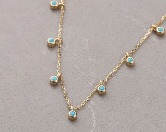May include: A gold chain necklace with turquoise stones hanging from it. The necklace is on a gray background.