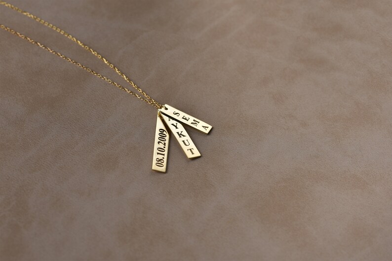 May include: Gold necklace with three rectangular pendants. The pendants are engraved with the names "Sena", "Ykut", and the date "08.10.2009".