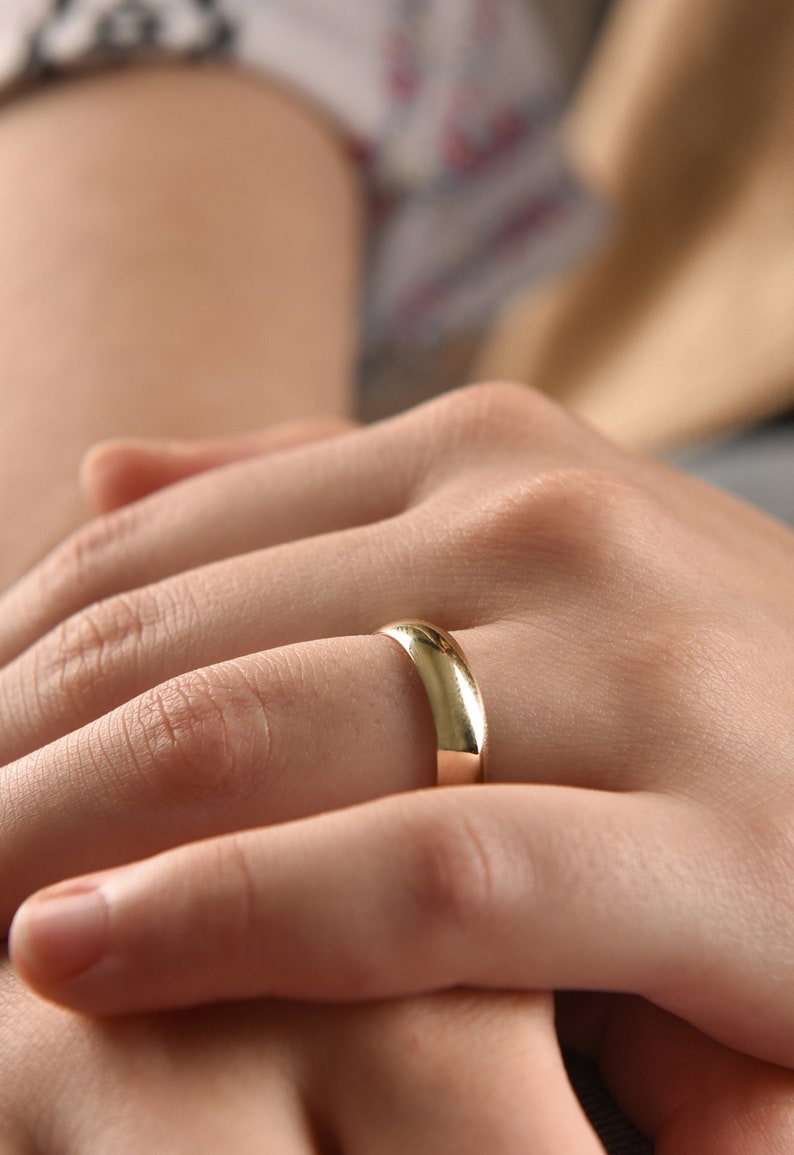 May include: A close-up of a person's hand wearing a simple gold wedding band.