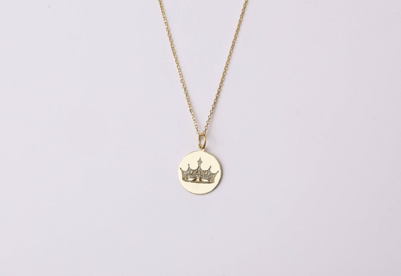 May include: A gold chain necklace with a round pendant featuring a crown design with small clear stones.