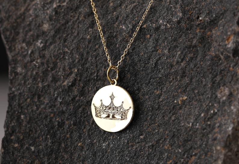 May include: A gold chain necklace with a round pendant featuring an engraved crown design.