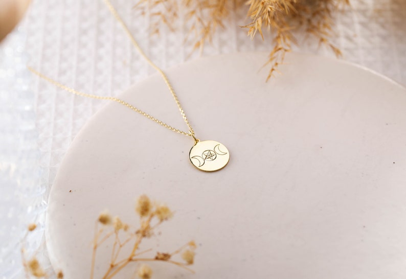 May include: Gold necklace with a round pendant featuring a triple moon and pentacle design.