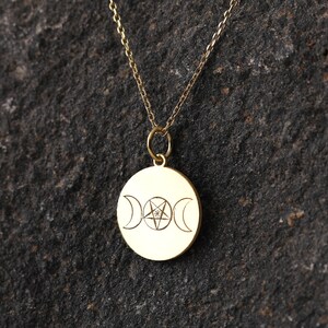 May include: A gold necklace with a round pendant featuring a triple moon symbol and a pentagram with a small diamond in the center.