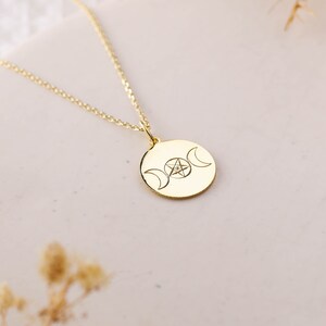 May include: A gold necklace with a round pendant featuring a triple moon symbol and a pentagram with a small diamond in the center.