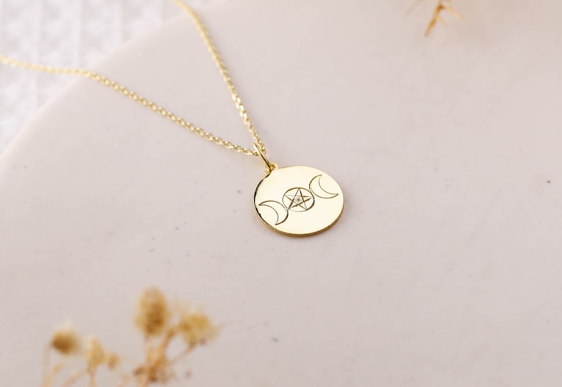 May include: A gold necklace with a round pendant featuring a triple moon symbol and a pentagram with a small diamond in the center.