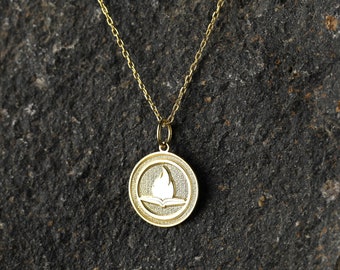 May include: A gold necklace with a round pendant featuring a stylised image of a book with a flame rising from it.
