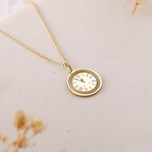 May include: A gold necklace with a round clock pendant featuring Roman numeral markings.