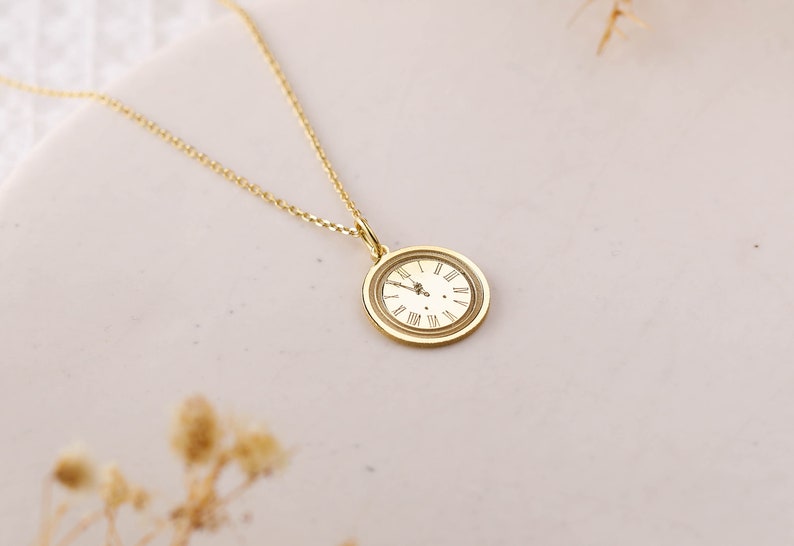 May include: A gold necklace with a round clock pendant featuring Roman numeral markings.
