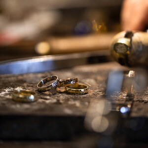 May include: Close-up of four gold and silver rings stacked on a rough, brown surface. The rings are different widths and have a hammered texture.