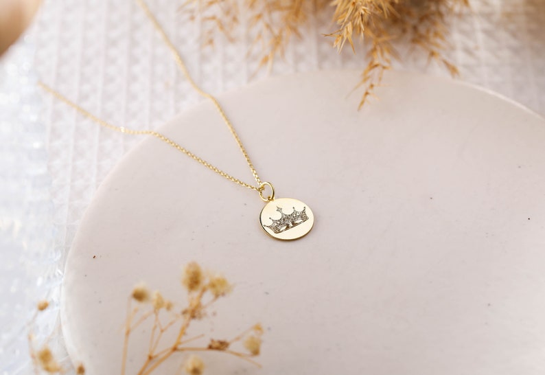 May include: A gold chain necklace with a round pendant featuring a crown design. The crown is made of small, sparkling stones.