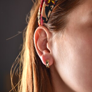May include: A close-up of a person's ear with a gold hoop earring. The earring is a simple, thin hoop with a slightly squared shape.