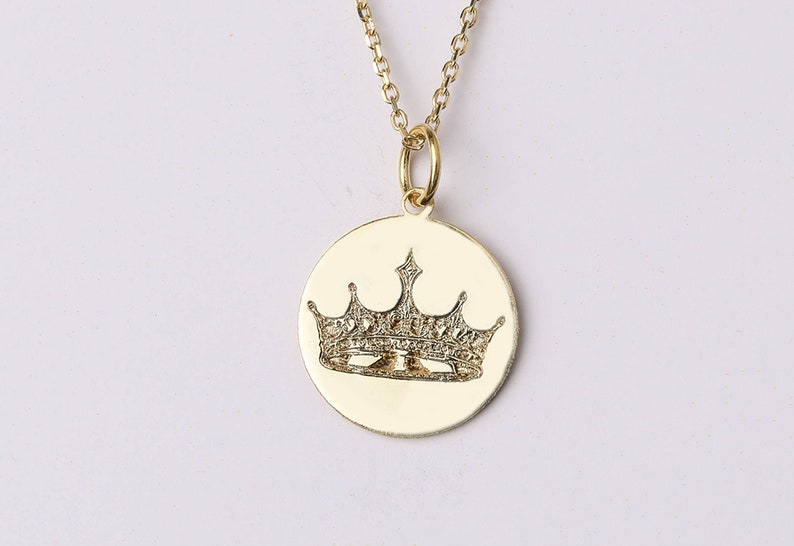 May include: A gold pendant necklace with a round charm featuring a detailed crown design with small diamonds.