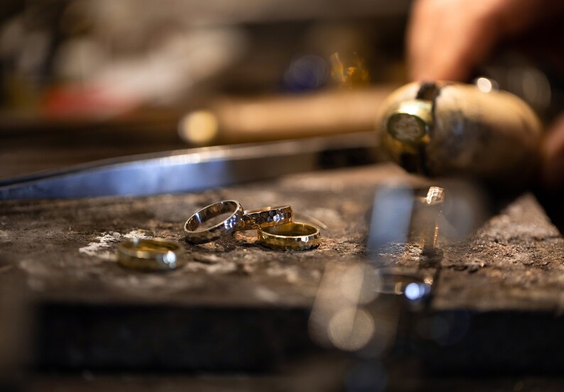 May include: Close-up of four gold and silver rings stacked on a rough, brown surface. The rings are different widths and have a hammered texture.