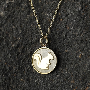 May include: A gold chain necklace with a round pendant featuring a white silhouette of a squirrel.
