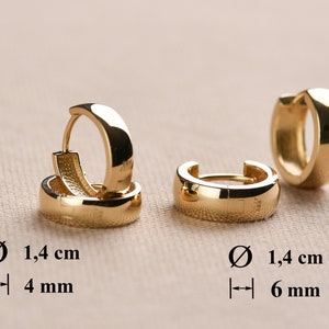 May include: Two pairs of gold hoop earrings. The earrings are 1.4 cm in diameter and have a width of 4 mm and 6 mm.