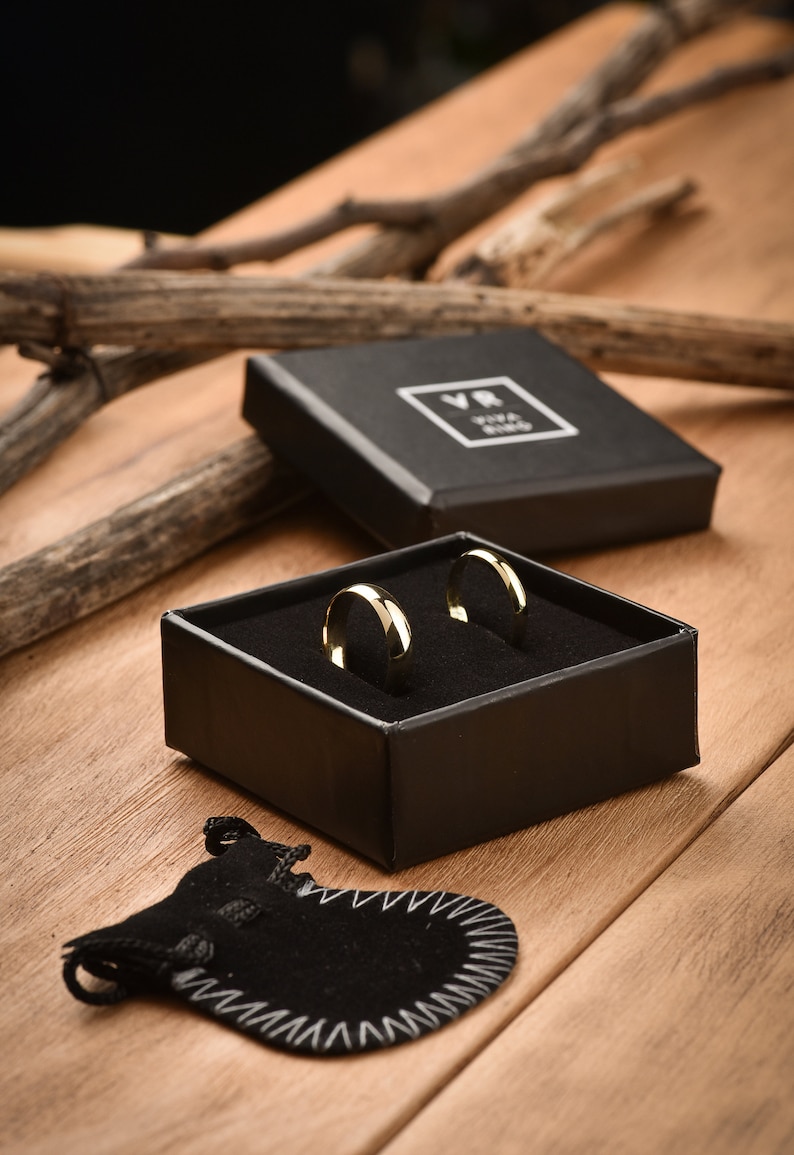 May include: Two gold wedding bands in a black velvet ring box with a black velvet pouch. The box has the text "VR Viva Ring" on the top.