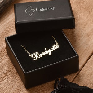 May include: A gold-colored necklace with the name "Bridgette" spelled out in cursive script. The necklace is in a black box with the word "bejewellike" printed on the top.