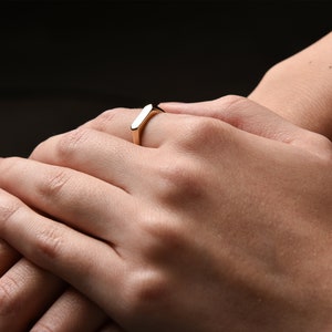 May include: A gold band ring with a flat, rectangular top.