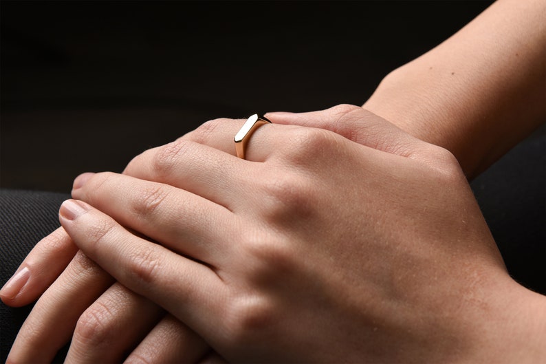 May include: A gold band ring with a flat, rectangular top.