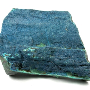 May include: A rough-hewn mineral specimen with a layered texture. The surface is a deep teal blue with areas of lighter turquoise and hints of green. The overall shape is irregular, showcasing the natural formation of the stone.