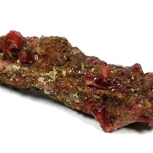 May include: A rough, reddish-brown mineral specimen with clusters of deep red, crystalline formations. The mineral has a textured surface and is set against a white background, highlighting its natural beauty. This specimen is a unique piece for collectors.
