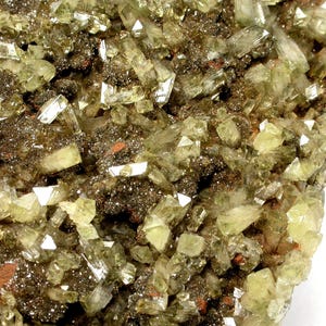 Könnte beinhalten: Nahaufnahme einer Mineralprobe mit zahlreichen hellgrünen, durchscheinenden Kristallen. Diese Kristalle sind in einer dunkelbraunen und rotbraunen Matrix eingebettet, wodurch eine strukturierte Oberfläche entsteht. Die Kristalle haben ein glasartiges Aussehen.