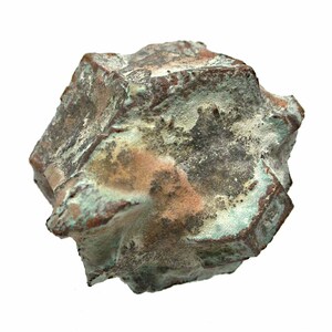 Op de afbeelding: Een verweerde, geometrische sculptuur met een ruw, getextureerd oppervlak. Het object toont een mix van kleuren, waaronder bruintinten, groen en hints van oranje. De algemene vorm is hoekig en onregelmatig, wat wijst op een natuurlijke of verouderde esthetiek.