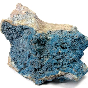 May include: A natural mineral specimen featuring a rough, textured surface. The rock displays a striking contrast of colors, with a vibrant blue hue covering a significant portion and a tan and gray base. The overall shape is irregular and organic.