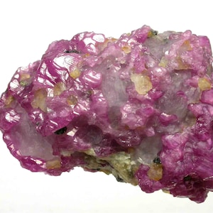 May include: A raw mineral specimen featuring clusters of vibrant magenta-coloured crystals. The structure displays a rough, crystalline texture with translucent light-coloured inclusions and small dark spots embedded within the bright pink formation.