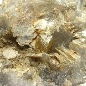 Puede incluir: Primer plano de un espécimen mineral con estructuras cristalinas en capas, translúcidas y opacas. Los colores varían del amarillo pálido al gris y blanco, con un aspecto brillante y reflectante. Se trata de una formación rocosa natural.