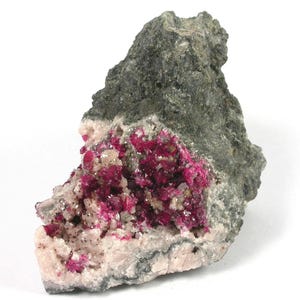 Puede incluir: Un espécimen mineral natural con una matriz de roca gris oscuro y un vibrante grupo de cristales de color rosa intenso. Los cristales están ubicados dentro de una base rosa claro y blanca, creando un contraste llamativo.