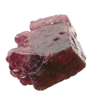 May include: A raw, deep red garnet crystal with a multifaceted, irregular geometric shape. The surface of the mineral displays a mix of smooth, reflective planes and textured, pitted areas, showcasing a translucent, dark crimson coloration throughout.