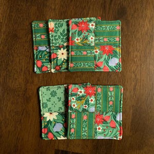 May include: Set of six green and red fabric coasters with a floral and striped pattern. The coasters are square and have a quilted texture.