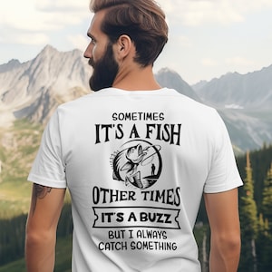 May include: White t-shirt with a black graphic design featuring a fish on a hook, a fisherman, and the text "Sometimes it's a fish, other times it's a buzz, but I always catch something."
