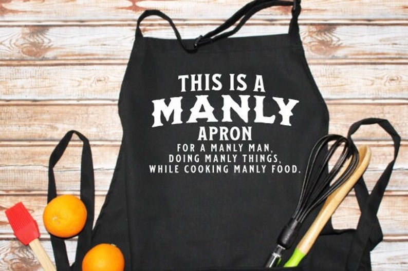 May include: Black apron with white text that reads "This is a Manly Apron for a Manly Man, Doing Manly Things, While Cooking Manly Food."