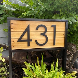May include: A wooden house number sign with black metal framing and black metal numbers. The sign displays the number 431.