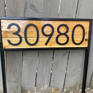 May include: Black metal frame with a wooden sign displaying the house number 30980. The sign is made of reclaimed wood and has a rustic look.