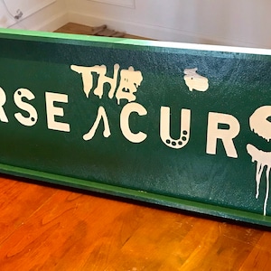 Peut inclure: Une enseigne en bois vert avec des lettres blanches qui disent "The Reverse Curse". L'enseigne est encadrée d'un cadre en bois vert foncé et porte une petite inscription "MDC" dans le coin inférieur droit.