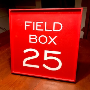 May include: Red wooden sign with white text that reads "FIELD BOX 25".
