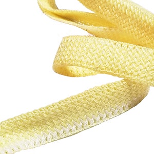 May include: A length of pale yellow woven ribbon, spiraling against a white background. The ribbon has a textured, basketweave pattern, and the edges are slightly lighter in color. The overall effect is soft and delicate.