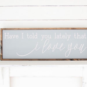 May include: A gray wooden sign with a brown frame, featuring the text "Have I told you lately that I love you" in white cursive lettering.