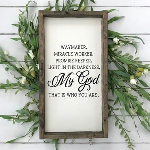 May include: A wooden sign with a white background and black text. The text reads "WAYMAKER, MIRACLE WORKER, PROMISE KEEPER, LIGHT IN THE DARKNESS, My God THAT IS WHO YOU ARE."