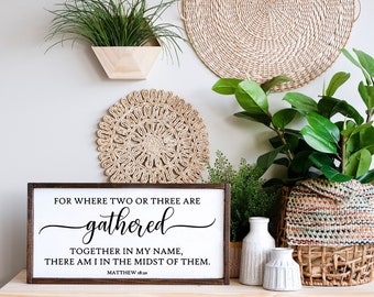 May include: A wooden sign with a brown frame and white background. The sign features a black and white quote from the Bible, Matthew 18:20, which reads "For where two or three are gathered together in my name, there am I in the midst of them."