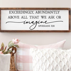 May include: A rectangular wooden framed wall sign with a white background featuring the black text: EXCEEDINGLY, ABUNDANTLY ABOVE ALL THAT WE ASK OR imagine EPHESIANS 3:20. The frame is a dark brown wood with a visible grain and smooth finish.
