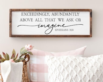 May include: A rectangular wooden framed wall sign with a white background featuring the black text: EXCEEDINGLY, ABUNDANTLY ABOVE ALL THAT WE ASK OR imagine EPHESIANS 3:20. The frame is a dark brown wood with a visible grain and smooth finish.